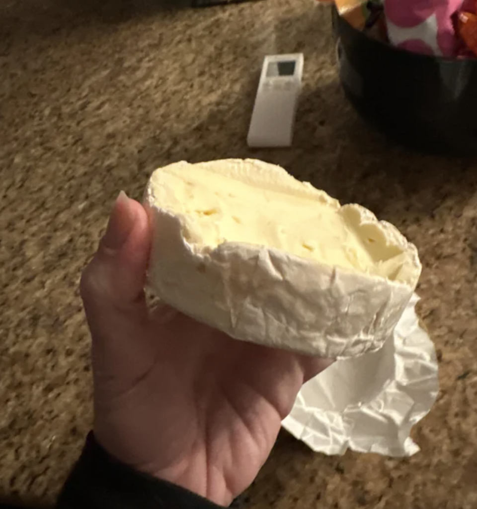 A person is holding a block of brie