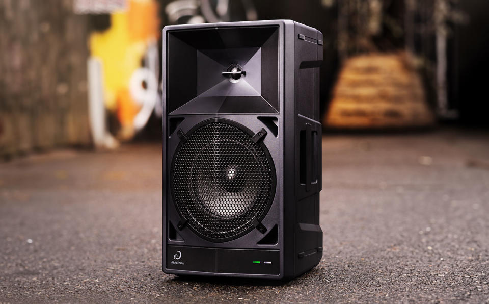 A black AlphaTheta Wave-Eight speaker sits in the middle of a paved backyard.