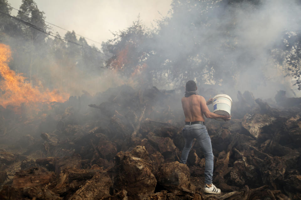 A local resident uses a bucket to try to stop a forest fire from reaching houses in the village of Figueiras, outside Leiria, central Portugal, Tuesday, July 12, 2022. Hundreds of firefighters in Portugal continue to battle fires in the center of the country that forced the evacuation of dozens of people from their homes mostly in villages around Santarem, Leiria and Pombal. (AP Photo/Joao Henriques)