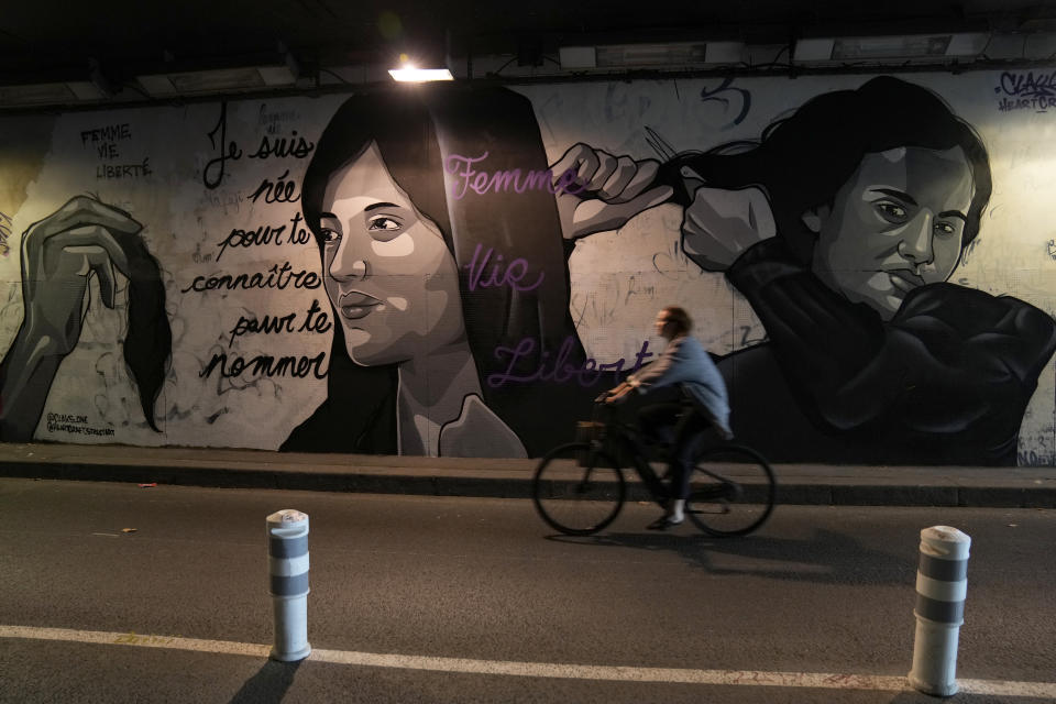 A woman rides bicycle front of a mural signed by Clacks-one and Heartcraft_Street art, depicting women cutting their hair to show support for Iranian protesters standing up to their leadership over the death of a young woman in police custody, in a tunnel in Paris, France, Wednesday, Oct. 5, 2022. Thousands of Iranians have taken to the streets over the last two weeks to protest the death of Mahsa Amini, a 22-year-old woman who had been detained by Iran's morality police in the capital of Tehran for allegedly not adhering to Iran's strict Islamic dress code. Mural reads : "I was born to know you to name you", "Woman Life Freedom".(AP Photo/Francois Mori)