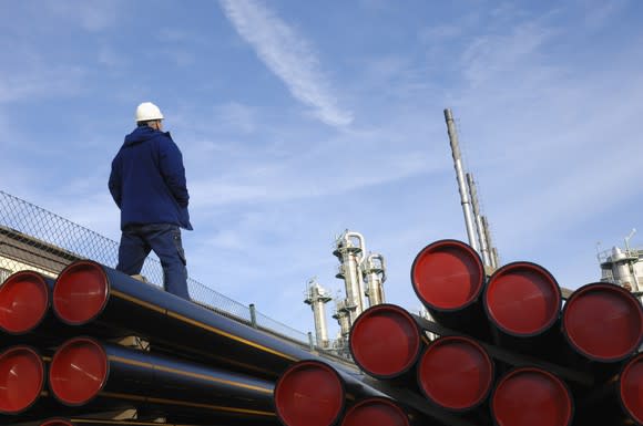 A person in a hard hat standing near a stack of pipes.