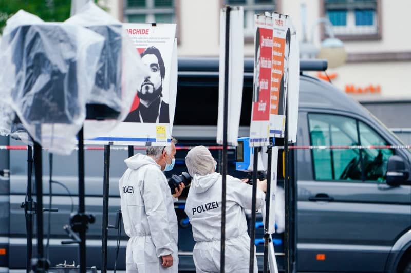 Forensic officers stand at a stall next to posters in the market square, where a knife-wielding attacker who injured several people in a market square in the southwestern German city of Mannheim has been shot by police.  Uwe Anspach/dpa