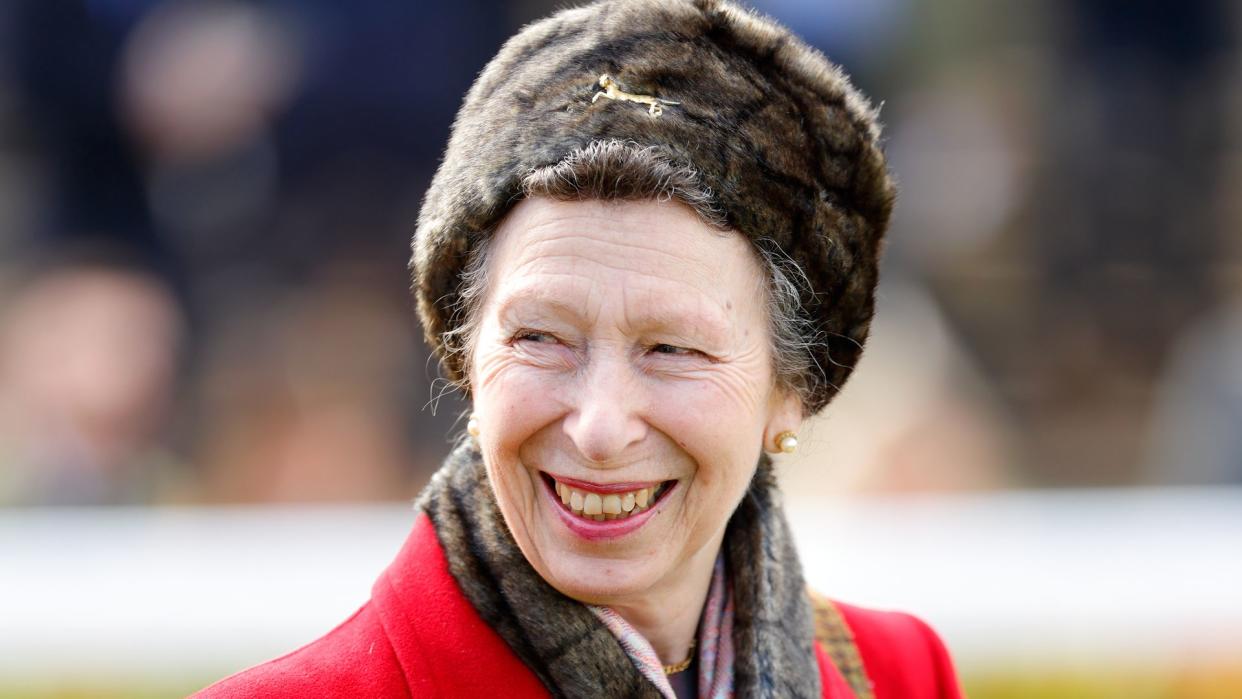 Princess Anne smiling in a red coat and furry hat