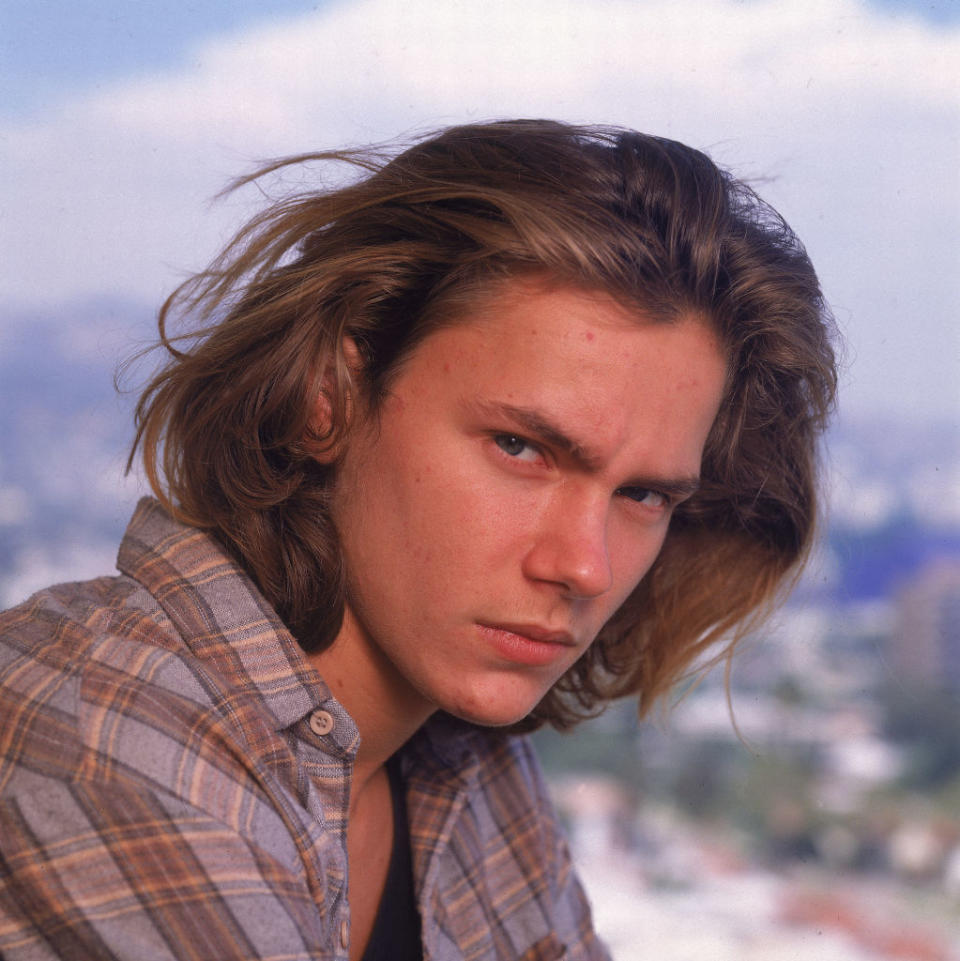 A portrait of River Phoenix with medium-length hair, wearing a plaid shirt