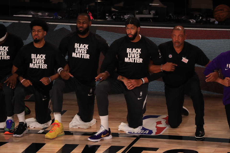 LeBron James y Anthony Davis hincan la rodilla en el suelo junto a sus compañeros de los Lakers durante la interpretación del himno estadounidense antes de su duelo ante los Clippers. (Foto: Mike Ehrmann / Getty Images).