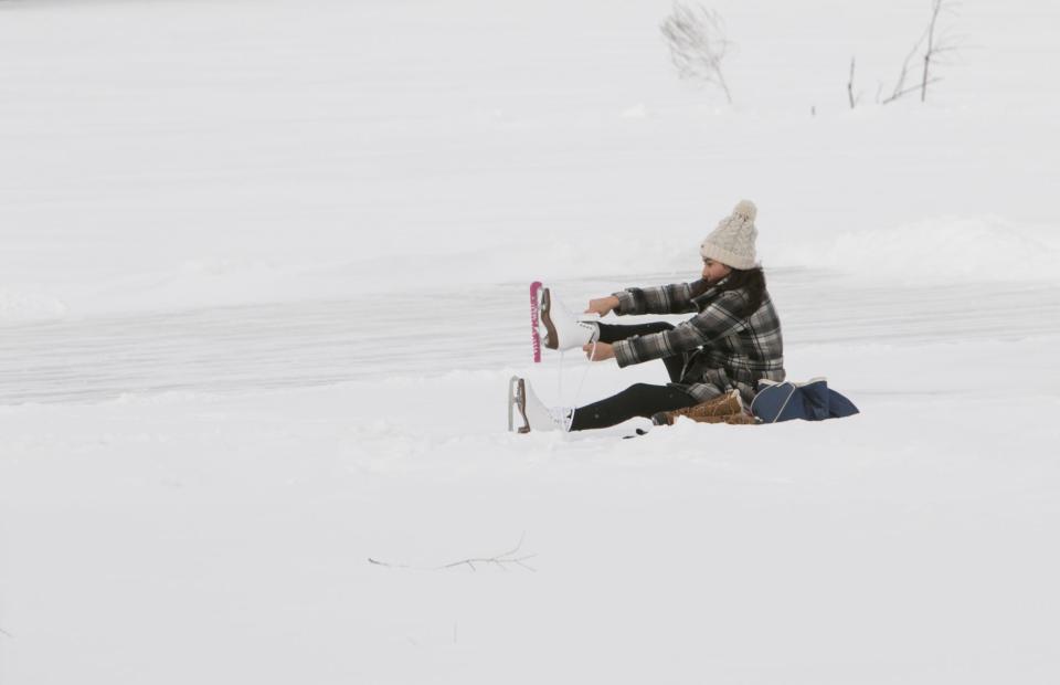 Kaylena Banghart of Genoa Township dons a pair of ice skates, having just shoveled off a patch of ice on Lake Chemung Monday, Feb. 15, 2021, as she learns to skate.