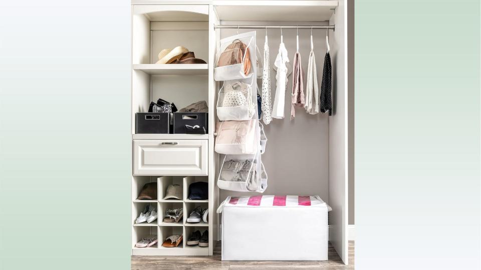 The purse organizer hanging from a closet rod surrounded by shoes, accessories and clothes. 