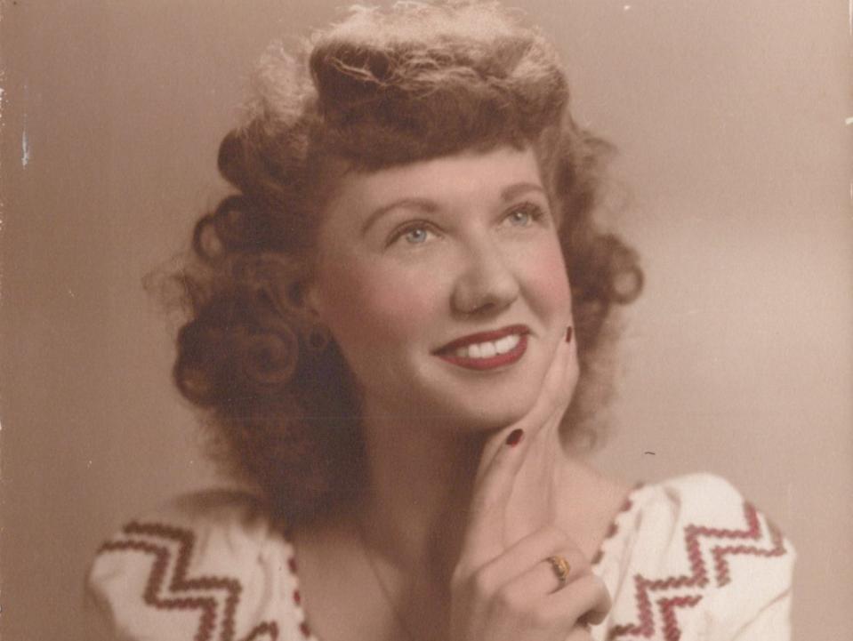 Jayne Burns appears in a colorized portrait as a young woman with her hand under her chin whilewearing a white puff-sleeved top.