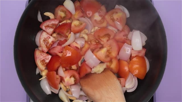 Cooking tomatoes, onion, cashew nuts, and grated garlic