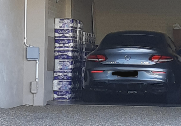 A Mercedes parked in a garage next to stacks of toilet paper.