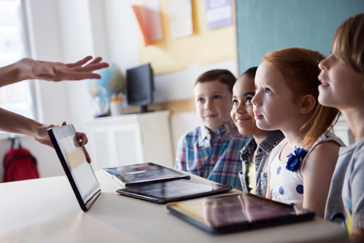 children listening to teacher with tablets in front of them