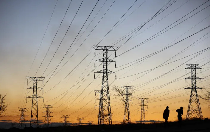 Locals walk past electricity pylons during frequent power outages from South African utility Eskom, caused by its aging coal-fired plants, in Soweto, South Africa, July 3, 2022. REUTERS/Siphiwe Sibeko