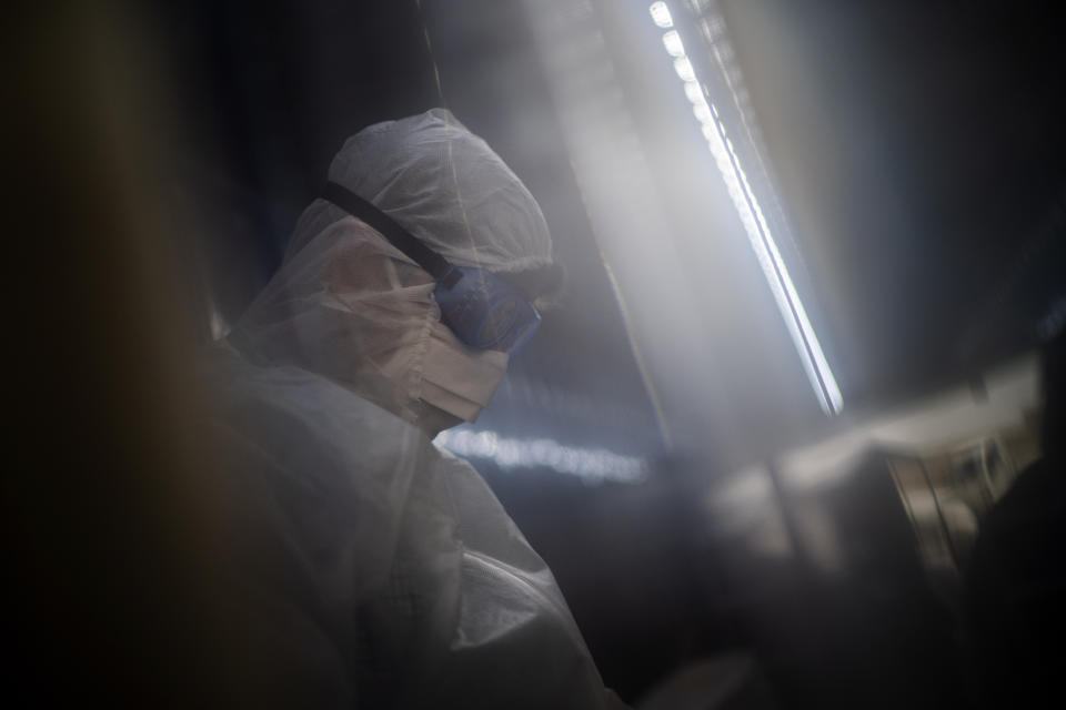 FILE- In this file photo dated Tuesday, Feb. 2, 2021, a mortuary employee wearing full PPE checks coffins containing the remains of COVID-19 victims in a refrigerated container in Johannesburg. The World Health Organization Monday Feb. 15, 2021, granted an emergency authorization to the coronavirus vaccine made by AstraZeneca, a move that should allow its partners to ship millions of doses to countries worldwide as part of a U.N.-backed program to stop the pandemic.(AP Photo/Jerome Delay, FILE)