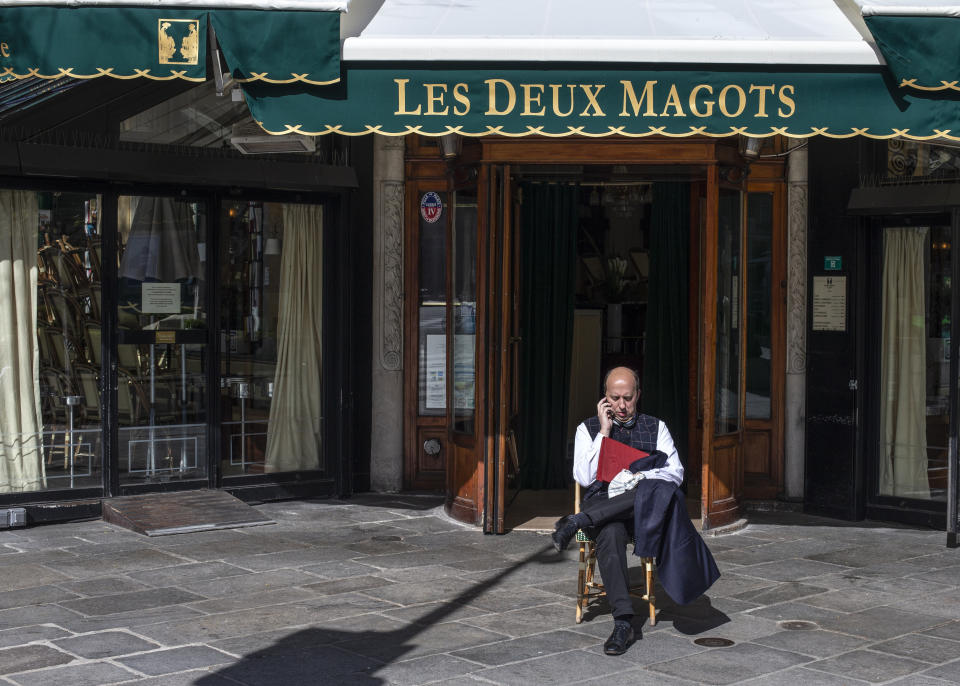 A man sits outside the closed famed Les Deux Magots cafe Sunday March 15, 2020 in Paris. French Prime Minister Edouard Philippe announced that France is shutting down all restaurants, cafes, cinemas and non-essential retail shops, starting Sunday, to combat the accelerated spread of the virus in the country. For most people, the new coronavirus causes only mild or moderate symptoms. For some it can cause more severe illness. (AP Photo/Rafael Yaghobzadeh)