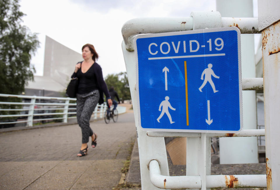 A woman walks past a social distancing sign, as the city with its surroundings face restrictions in an effort to avoid a local lockdown being forced upon the region to curb the spread of the coronavirus disease (COVID-19), in Manchester, Britain August 4, 2020. REUTERS/Molly Darlington