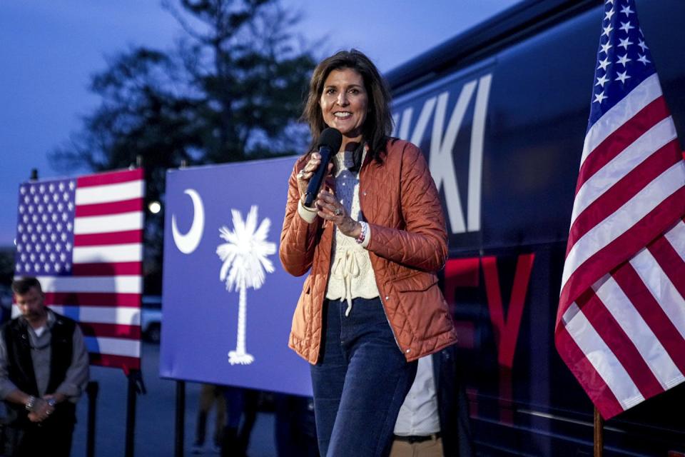 A woman stands on a stage holding a microphone in front of a U.S. flag and the South Carolina state flag.