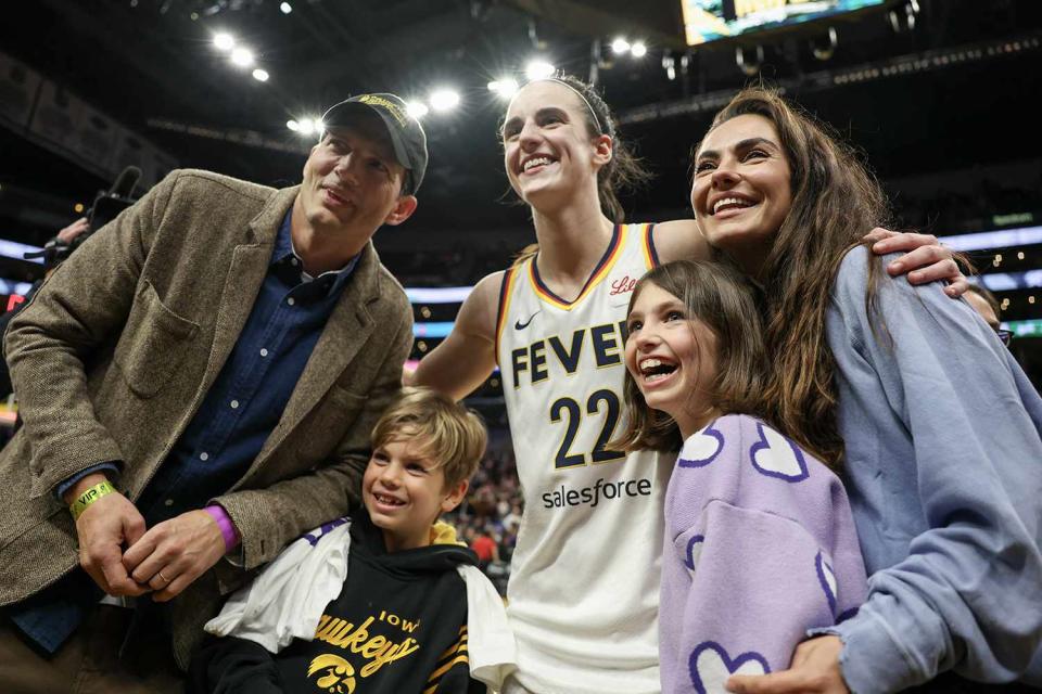 <p>Harry How/Getty Images</p> Ashton Kutcher, Mila Kunis and their two children with Caitlin Clark