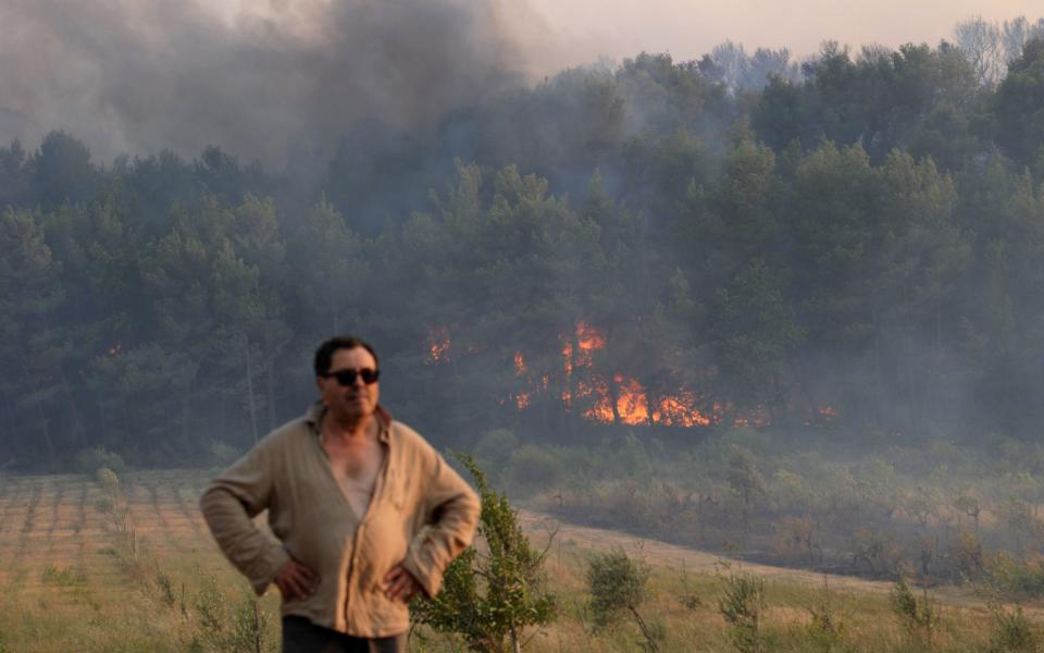 A man stands near a forest fire in Saint Cannat, near Aix en Provence, in the Bouches du Rhone region. - Credit:  FRANCK PENNANT/AFP