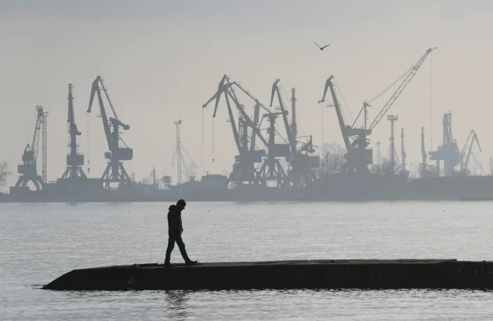 FILE - A man walks in front of harbor cranes at the port in Mariupol, Ukraine, Wednesday, Feb. 23, 2022. Mariupol, which is part of the industrial region in eastern Ukraine known as the Donbas, has been a key objective for Russia since the start of the Feb. 24 invasion. (AP Photo/Sergei Grits, File)