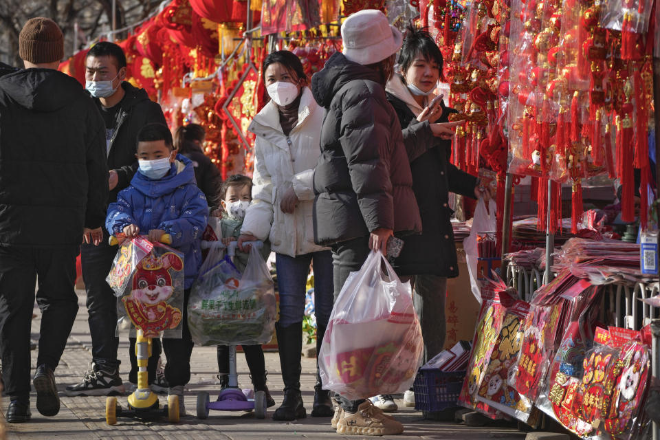 Children wearing face masks ride on their scooter with Chinese Year of the Rabbit decoration passing by residents shop for Chinese Lunar New Year decorations at a pavement stores in Beijing, Saturday, Jan. 7, 2023. China has suspended or closed the social media accounts of more than 1,000 critics of the government's policies on the COVID-19 outbreak, as the country moves to further open up. (AP Photo/Andy Wong)