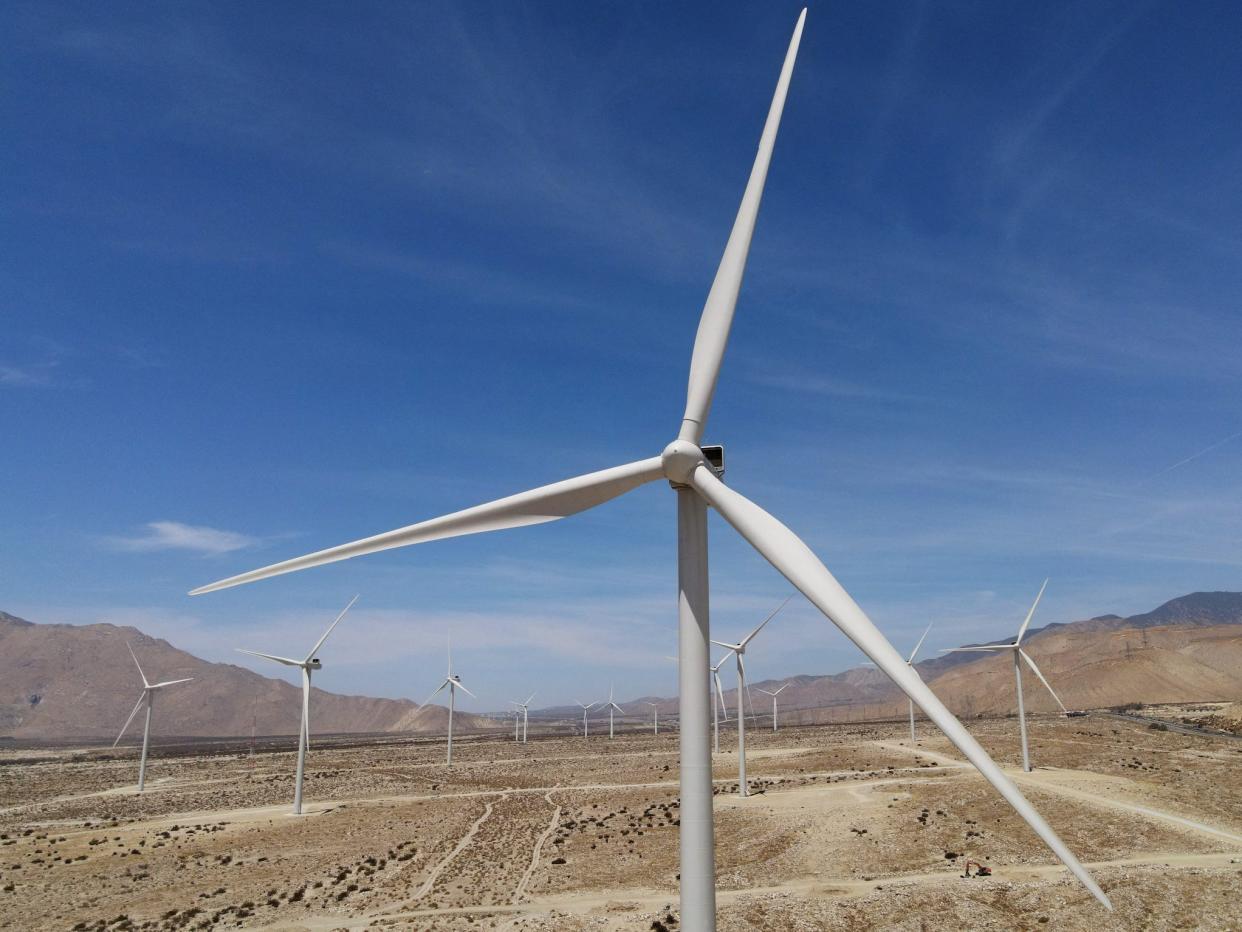 wind turbine in a field of turbines against blue sky mountains in the background