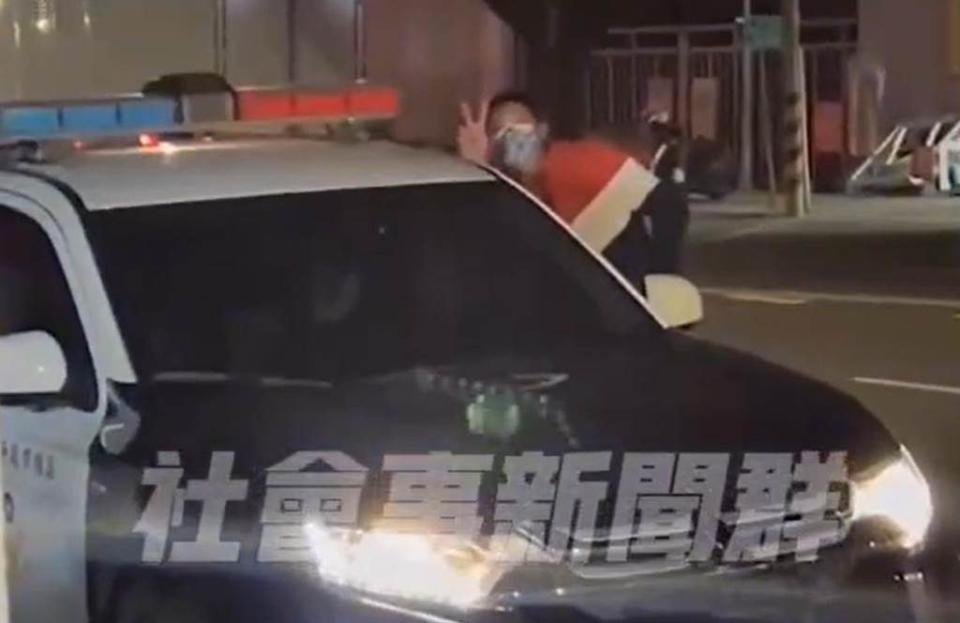  一名年輕男子，一步步走向駕駛座旁，甚至還對鏡頭比出「YA」的手勢，大膽地在警車旁嬉戲。圖取自社會事新聞群