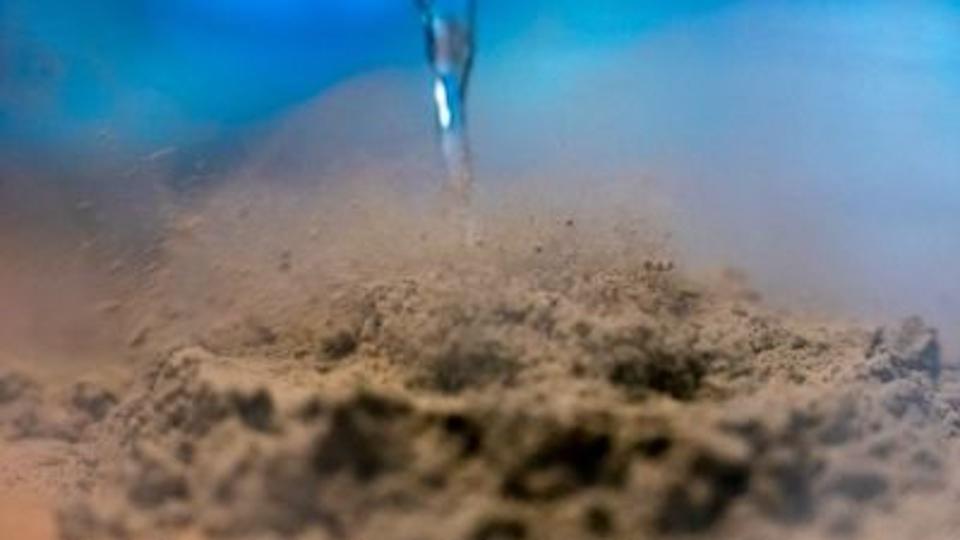 A close-up image of a dropper releasing liquid nitrogen on a pile of volcanic ash.