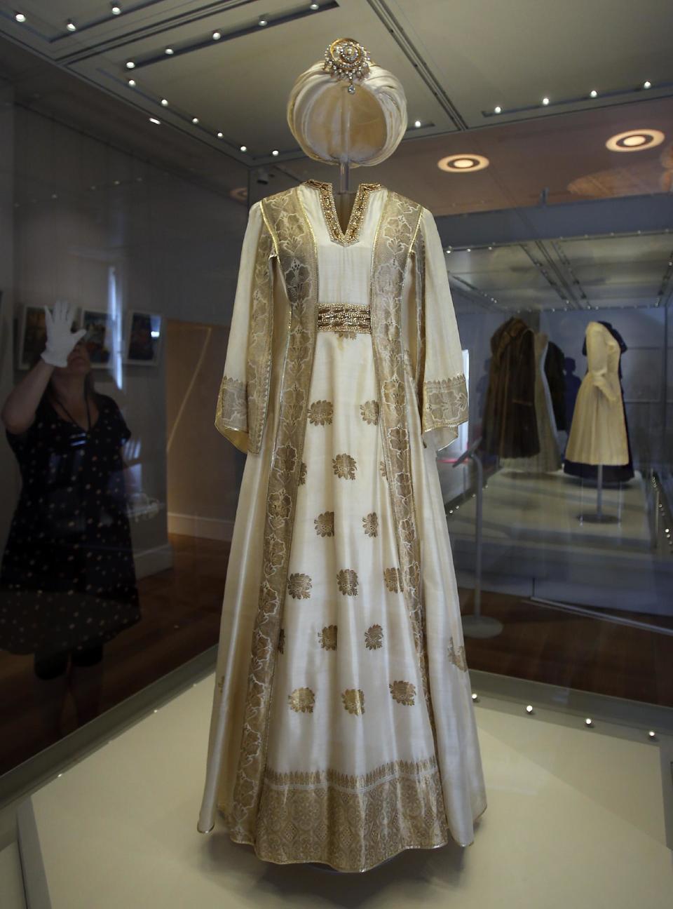 In this photo taken Monday, July 1, 2013, an employee cleans the glass cabinet showing a turban dress worn by Princess Margaret, at the Fashion Rules exhibition at Kensington Palace in London. Opening on 4 July, a new glamorous exhibit at Kensington Palace showcases how the styles of three royal ladies; Queen Elizabeth II, her sometimes risque sister Margaret, and the glamorous Princess Diana, each reflected and influenced the trends of their fashion heyday. (AP Photo/Frank Augstein)