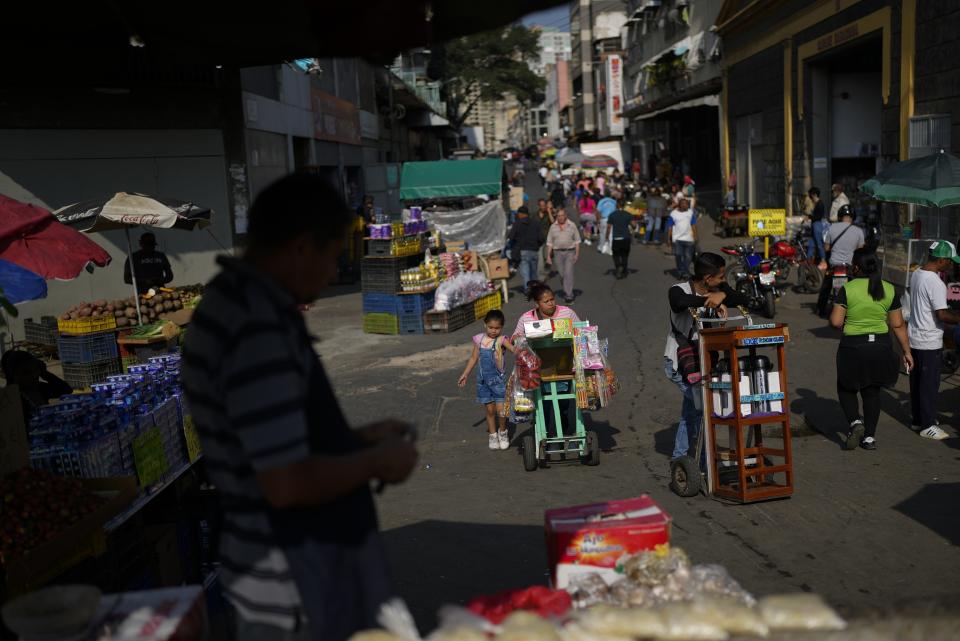 FILE - People walk near a market in Caracas, Venezuela, Tuesday, Feb. 28, 2023. A complex crisis continues to make food and other necessities unaffordable. (AP Photo/Ariana Cubillos, File)