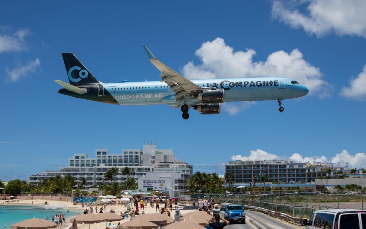 A sky blue La Compagnie plane flying over a beach in St. Maarten as it gets ready to land.