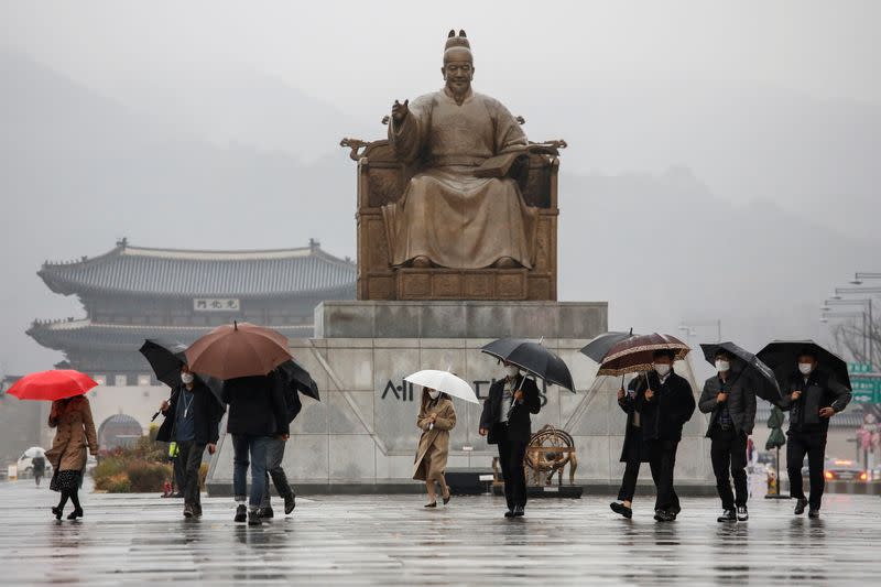 Pedestrians wearing masks walk with umbrellas as it rains amid the coronavirus disease (COVID-19) pandemic in central Seoul