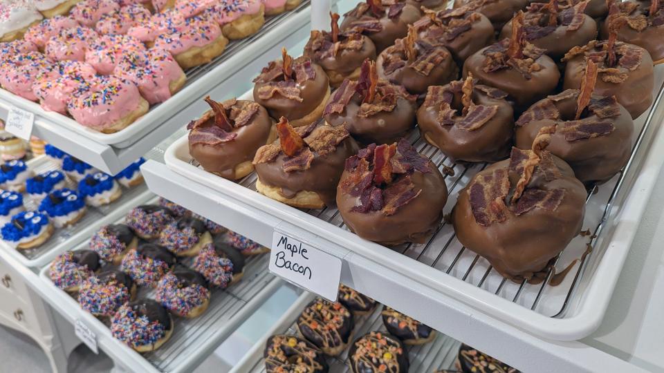 Maple bacon doughnuts share a shelf with more traditional pink icing and sprinkles at Decked Out Donuts.