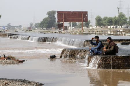 Flood victims sit by a damaged road as they look over floodwaters in Muzzafargarh, Punjab province September 15, 2014. REUTERS/Asim Tanveer