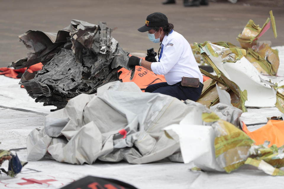 An investigator of the National Transportation Safety Committee inspects parts of aircraft's debris recovered from the Java Sea where a Sriwijaya Air passenger jet crashed, at Tanjung Priok Port, Tuesday, Jan. 12, 2021. Indonesian navy divers were searching through plane debris and seabed mud Tuesday looking for the black boxes of the Sriwijaya Air jet that nosedived into the Java Sea over the weekend with 62 people aboard. (AP Photo/Dita Alangkara)