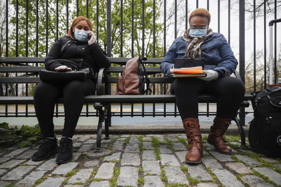 In this Thursday, April 23, 2020 photo, Ruth Caballero, a nurse with The Visiting Nurse Service of New York, right, and Catherine Peralta, her Spanish-language translator, sit next to an empty park as they have a teleconference with a patient during their rounds in upper Manhattan in New York. Home care nurses, aides and attendants, who normally help an estimated 12 million Americans with everything from bathing to IV medications, are now taking on the difficult and potentially dangerous task of caring for coronavirus patients. (AP Photo/John Minchillo)