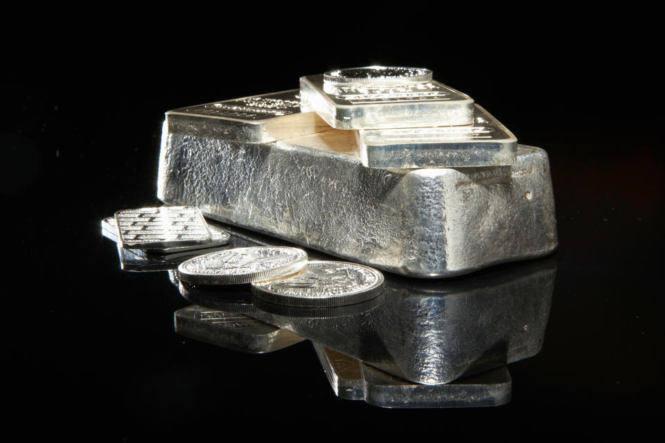Silver bars and coins on a flat surface against a dark background.