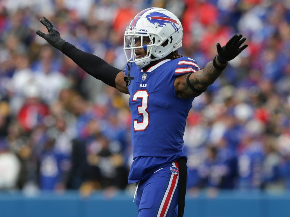 Damar Hamlin, attired in his Buffalo Bills jersey and helmet, holds his hands up as he walks on a football field.