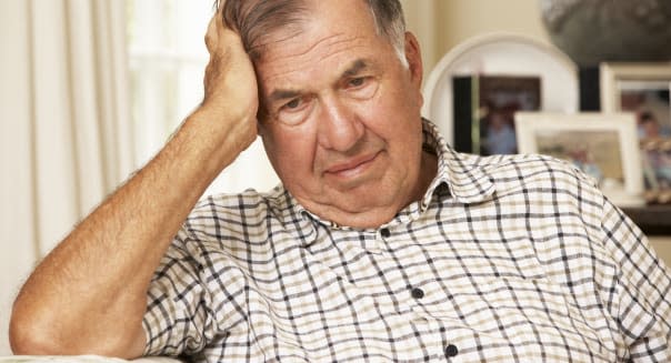 Unhappy Retired Senior Man Sitting On Sofa At Home