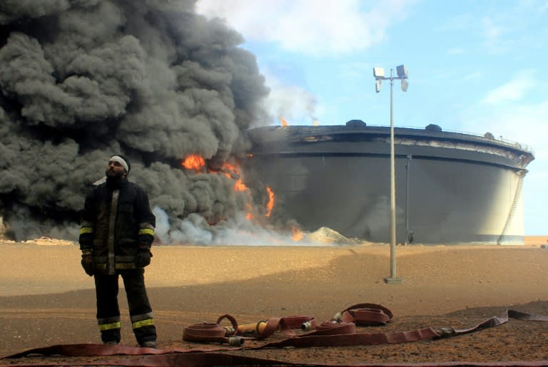 A Libyan fireman stands in front of smoke and flames rising from an oil storage tank in northern Libya's Ras Lanouf region on January 23, 2016, after it was set ablaze earlier in the week following attacks launched by the Islamic State group