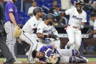 Miami Marlins' Otto Lopez picks up Bryan De La Cruz after De La Cruz collided with Colorado Rockies catcher Elias Díaz to score the winning run during the 10 inning of a baseball game, Tuesday, April 30, 2024, in Miami. The Marlins defeated the Rockies 7-6. (AP Photo/Marta Lavandier)