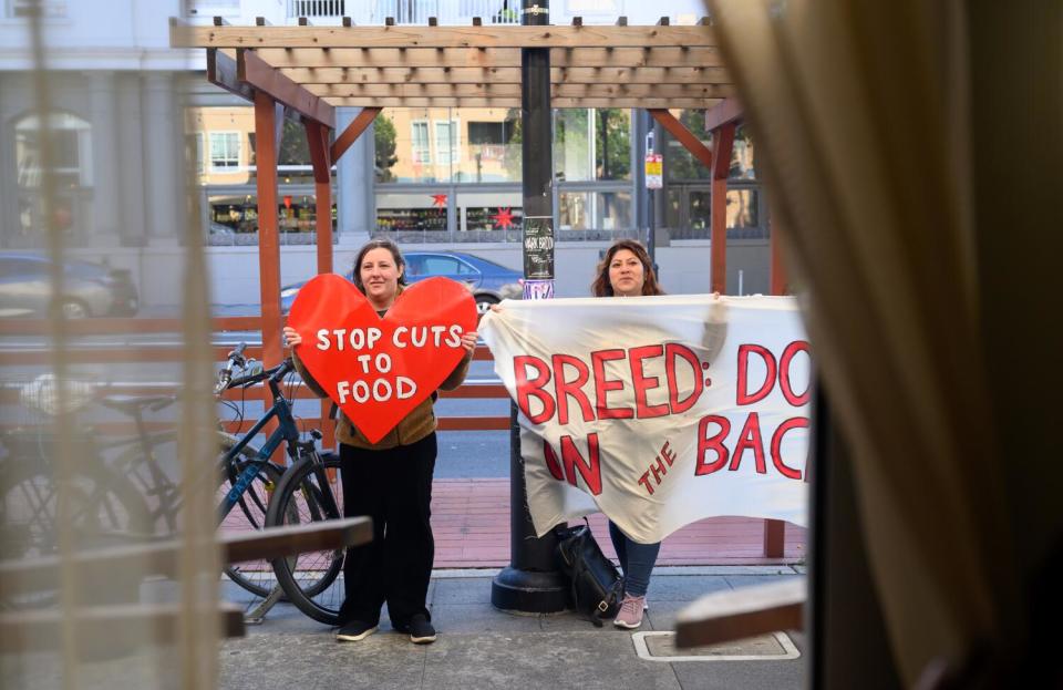 Protesters hold signs, including a sign that says, "Stop cuts to food"