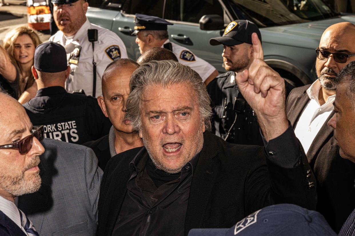 Steve Bannon stands in a group of people that includes police officers and holds up a finger and appears to be about to say something.