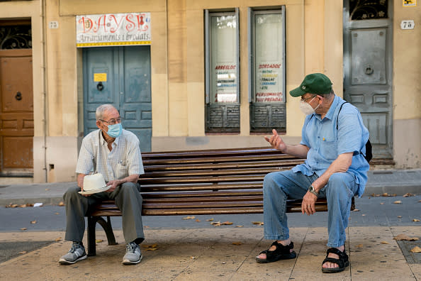 Two men talk on a bench keeping a safe distance and wearing a safety mask in Hospitalet de Llobregat, Spain. 