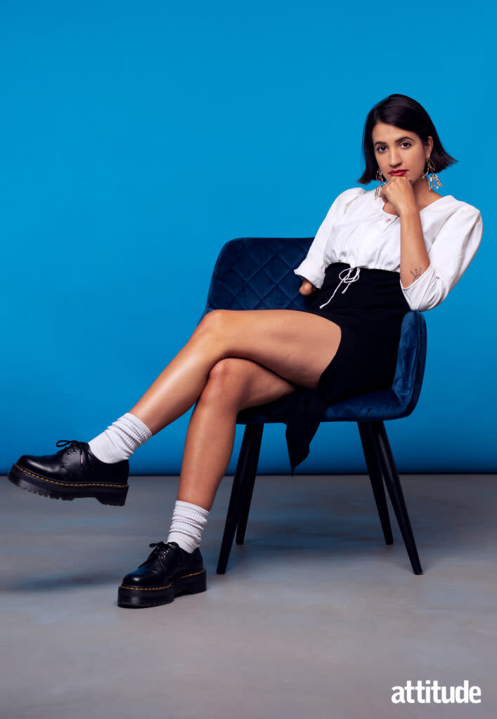 Image of Victoria Canal against a blue background. She's sat sideways on a dark blue chair.