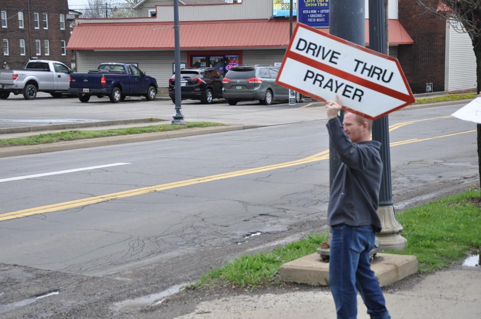 Rev. Todd Troyer, 41, the pastor at Alliance First Assembly of God Church, holds a sign welcoming people to participate in the church's drive-thru prayer service on Thursday, April 11, 2024.
