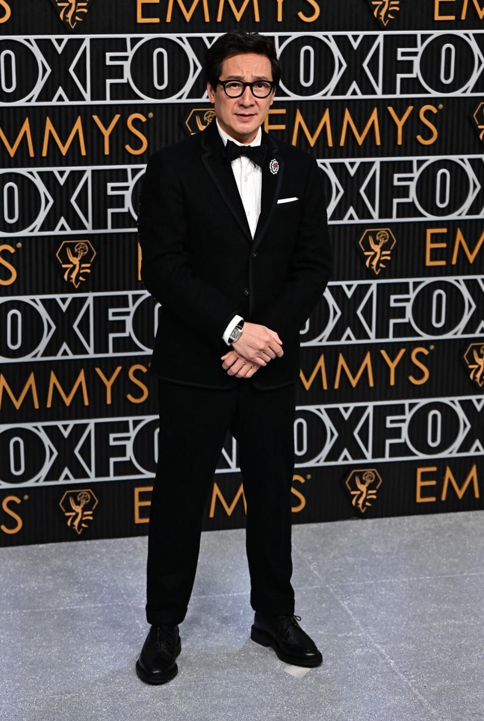 Everything Everywhere All At Once star Ke Huy Quan wears his signature thick-framed glasses and a classic tuxedo with a brooch at the 75th Emmy Awards.