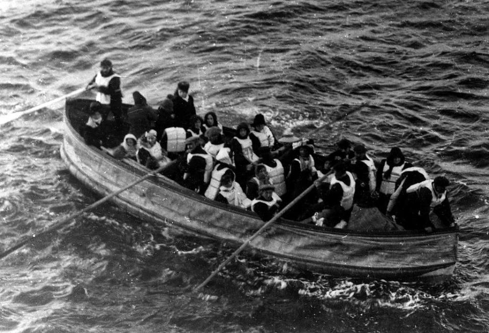 A lifeboat with about 20–25 people wearing life jackets in it