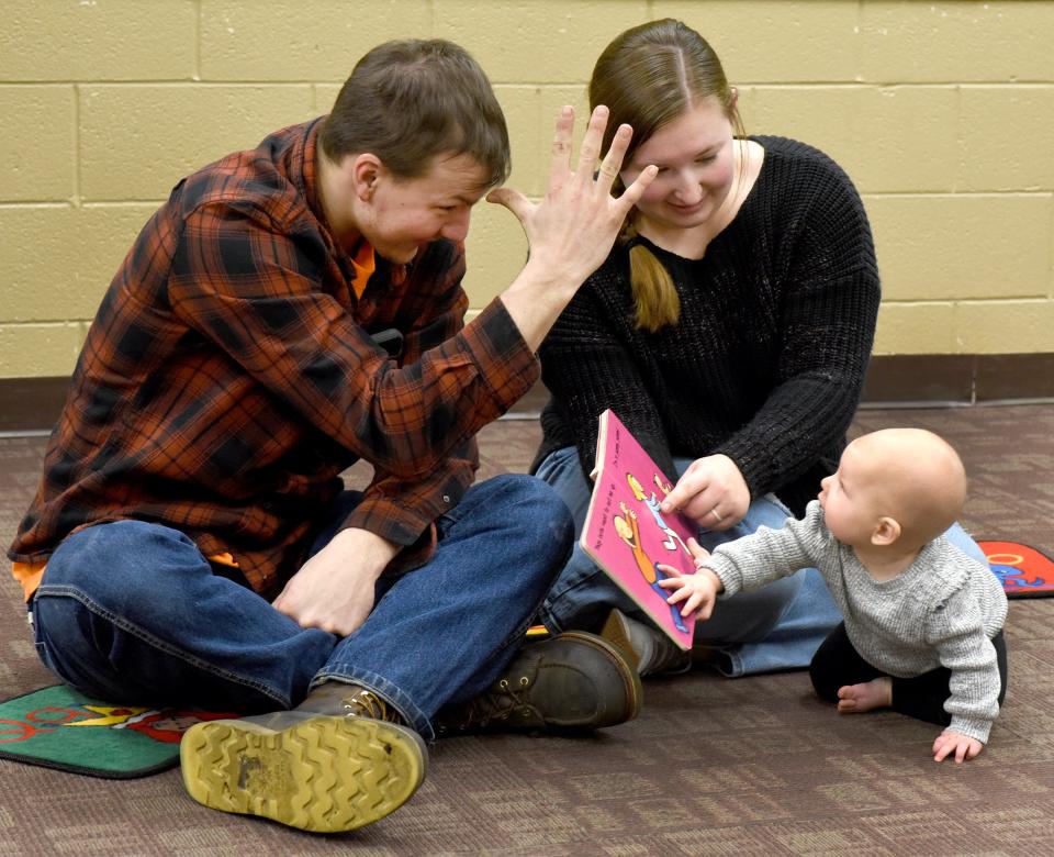 Riley Zimmerman puts his hand to his forehead to say "Dada" to his 7-month-old baby girl, Myla, as he and his wife, Layne, holding the book "Huggy Kitty," take part in the sign language class at Summerfield-Petersburg Branch Library with Sarah Seegert, the youth service technician. The couple were learning two new words, "Dada" and "Mama." The class is an 8-week introduction to using sign language with babies.