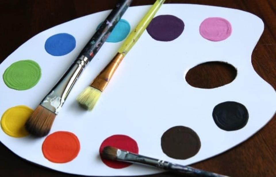 Cardboard paint palette with three brushes on top.