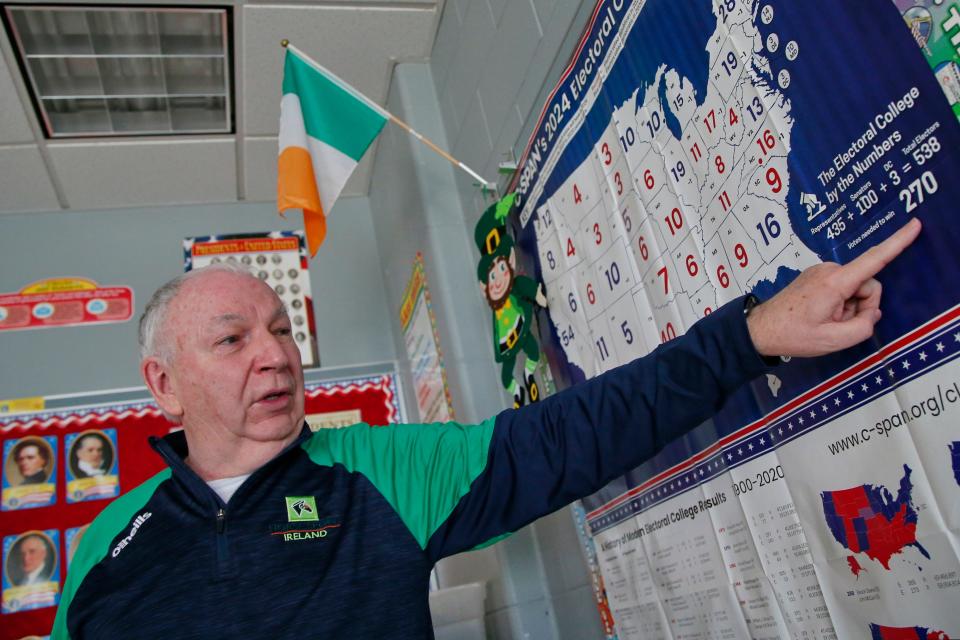 Christopher Donnelly, originally from Derry, Northern Ireland, points to how many electoral votes are required to win an election during his social studies class at the Normandin Middle School in New Bedford. Hanging from the wall an Irish flag.